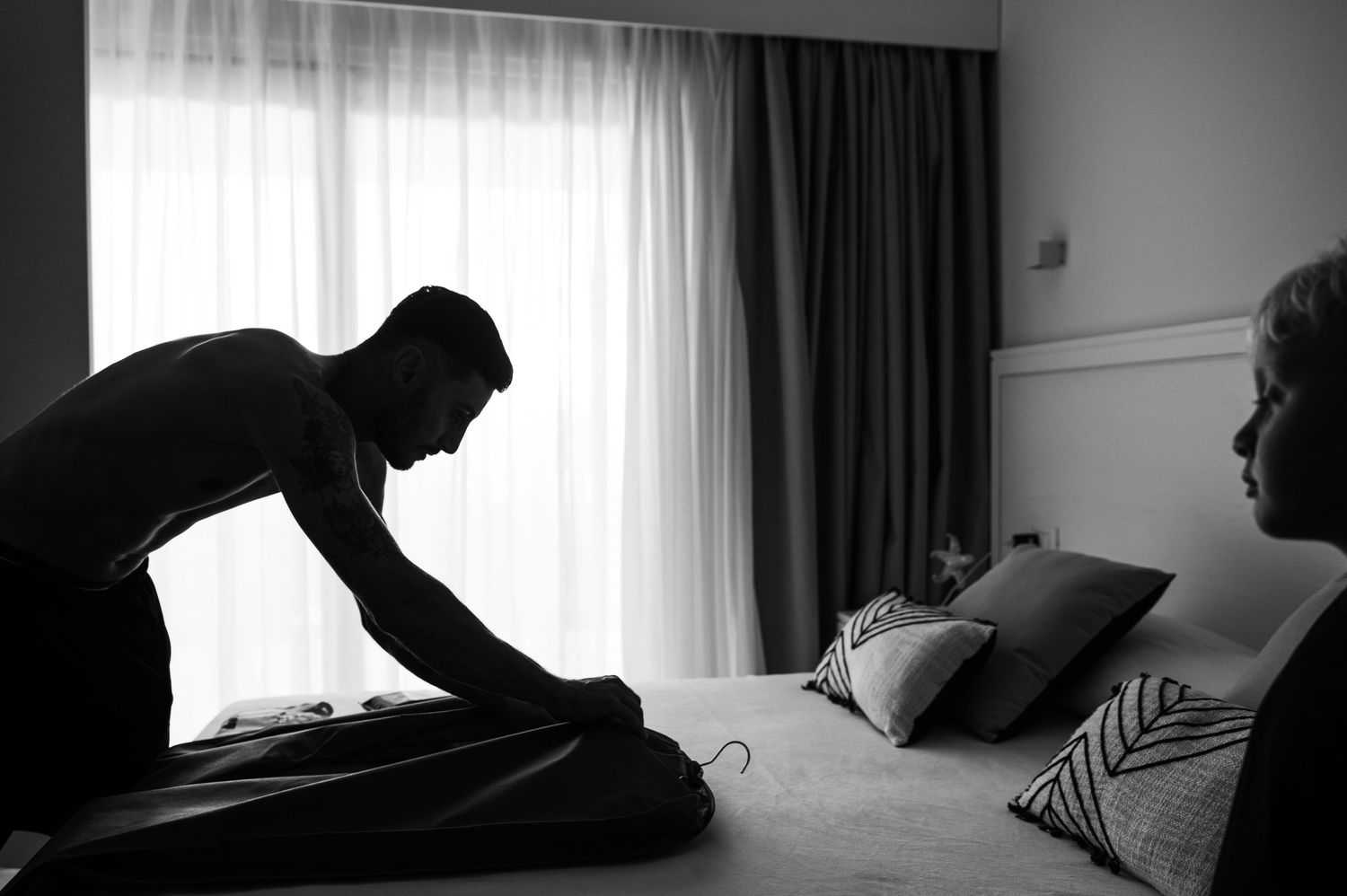 Dramatic black and white silhouettes through window light in a minimalist bedroom setting.
