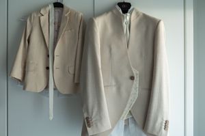 Row of light beige suits hanging neatly on clothing hangers against a pale wall.