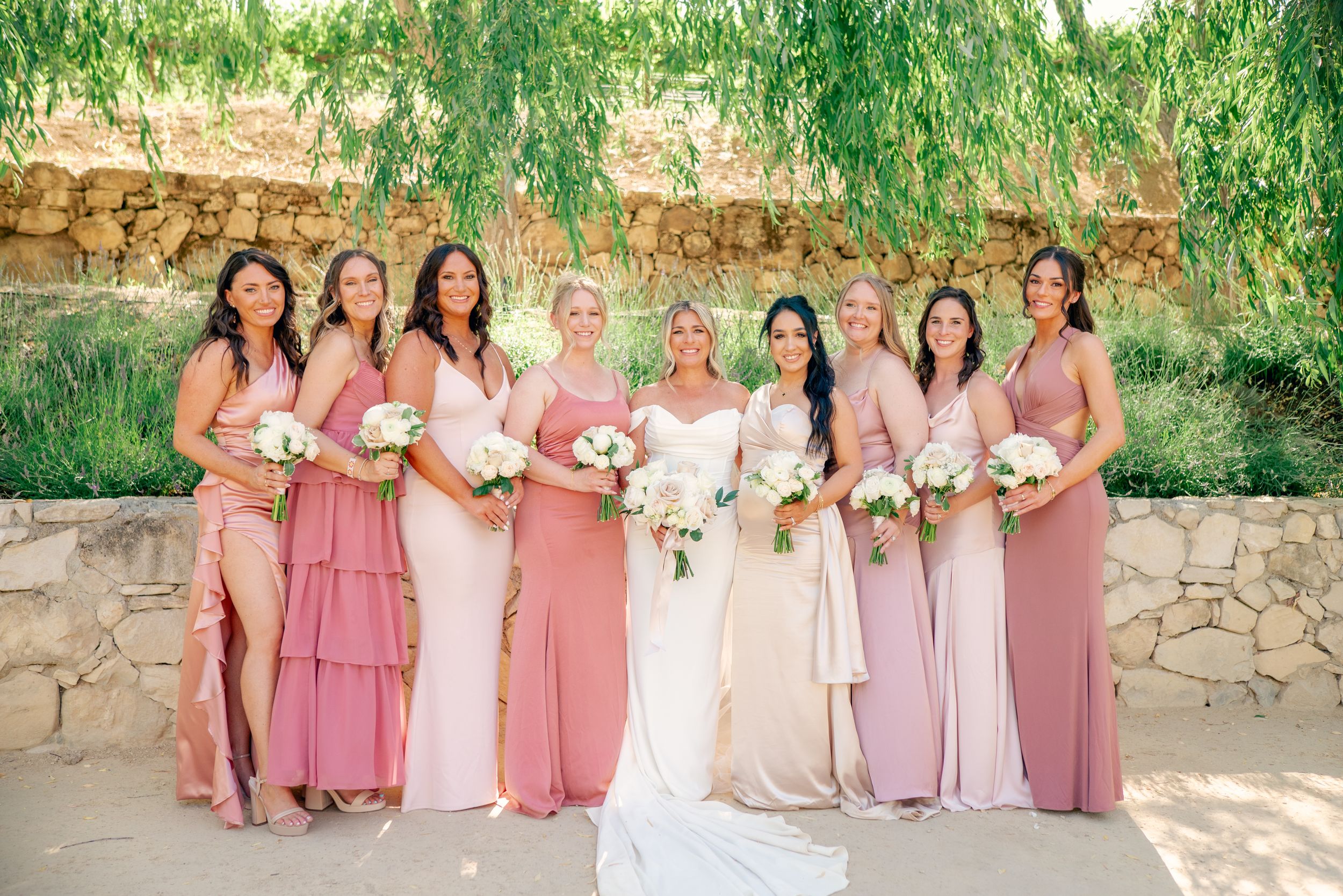 Wedding party in pink dresses posing under weeping willow trees.