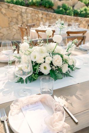 Elegant white floral centerpieces with roses and greenery on reception tables.