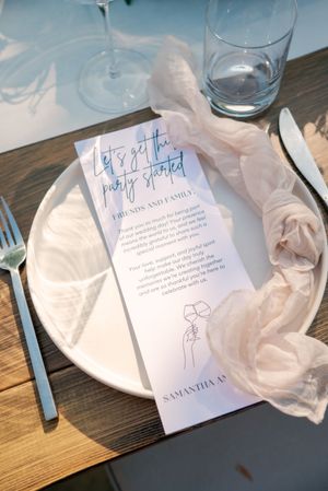 Wedding stationery and place settings in soft blue tones on wooden table.