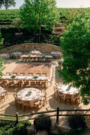 Aerial view of outdoor wedding reception setup with wooden chairs and white linens.