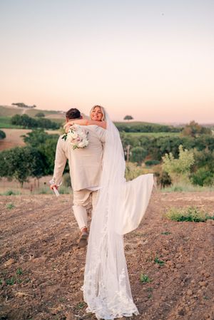 Wedding couple walking through golden hills during sunset with flowing white dress and veil.