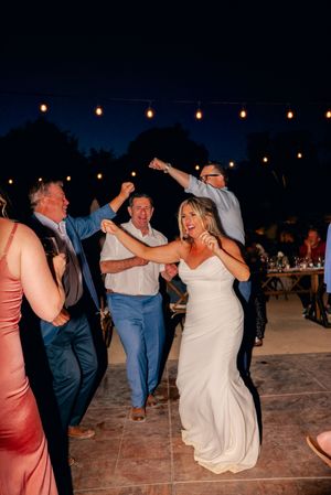 Wedding guests dancing joyfully at an outdoor evening reception under string lights.