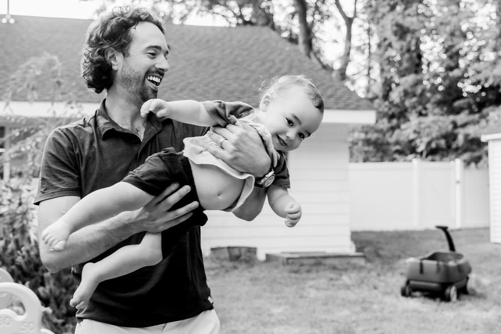 Candid family photography capturing a playful moment between a father and baby during an on-location session in Andover, MA.