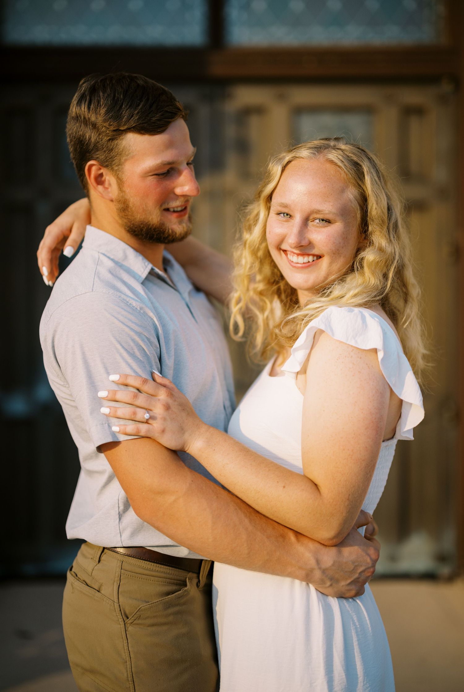 Happy couple shares a romantic moment while embracing in front of an ornate door during a warm sunset.