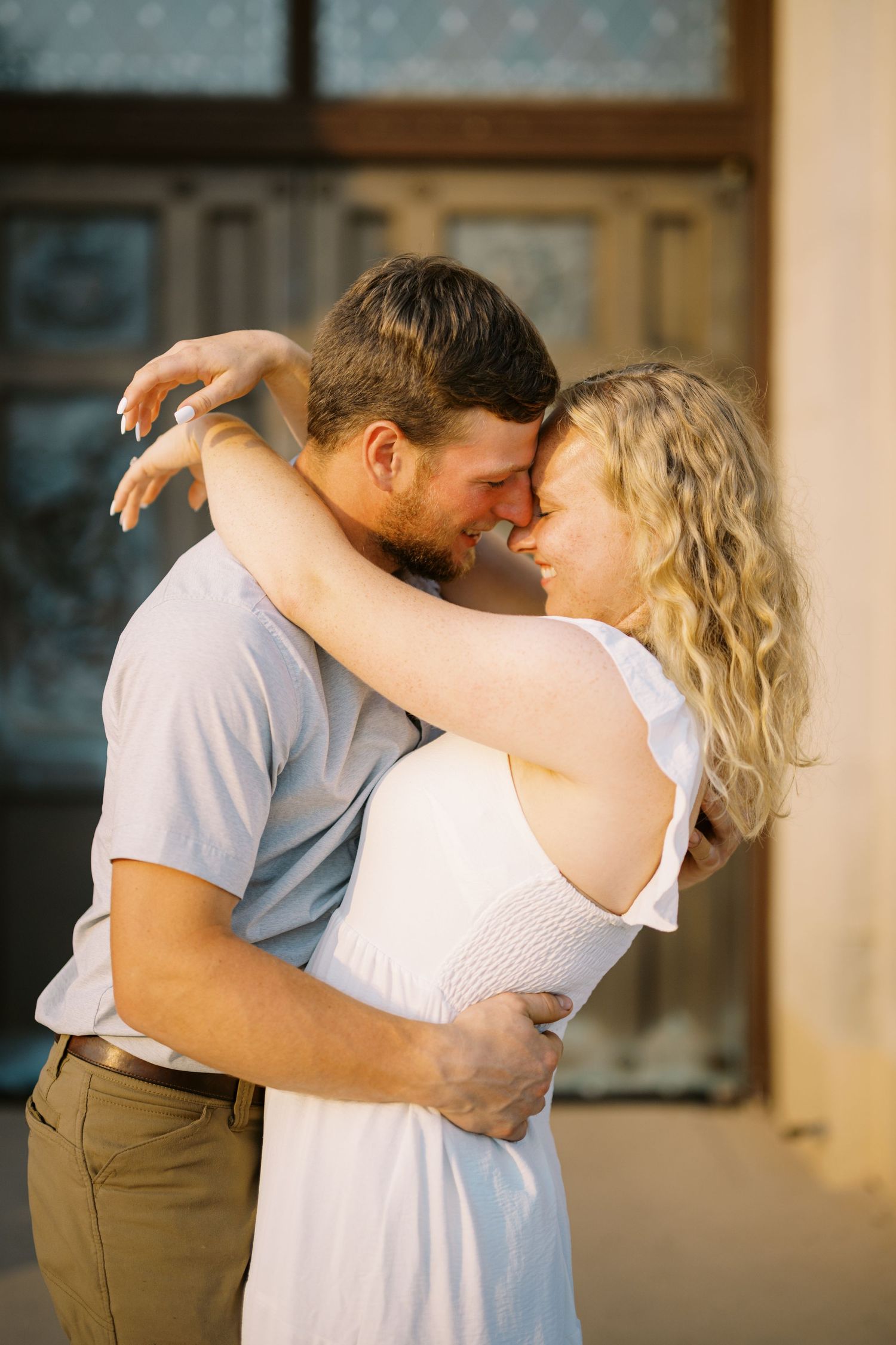 A romantic couple embraces intimately in a tender moment against a sunlit backdrop.