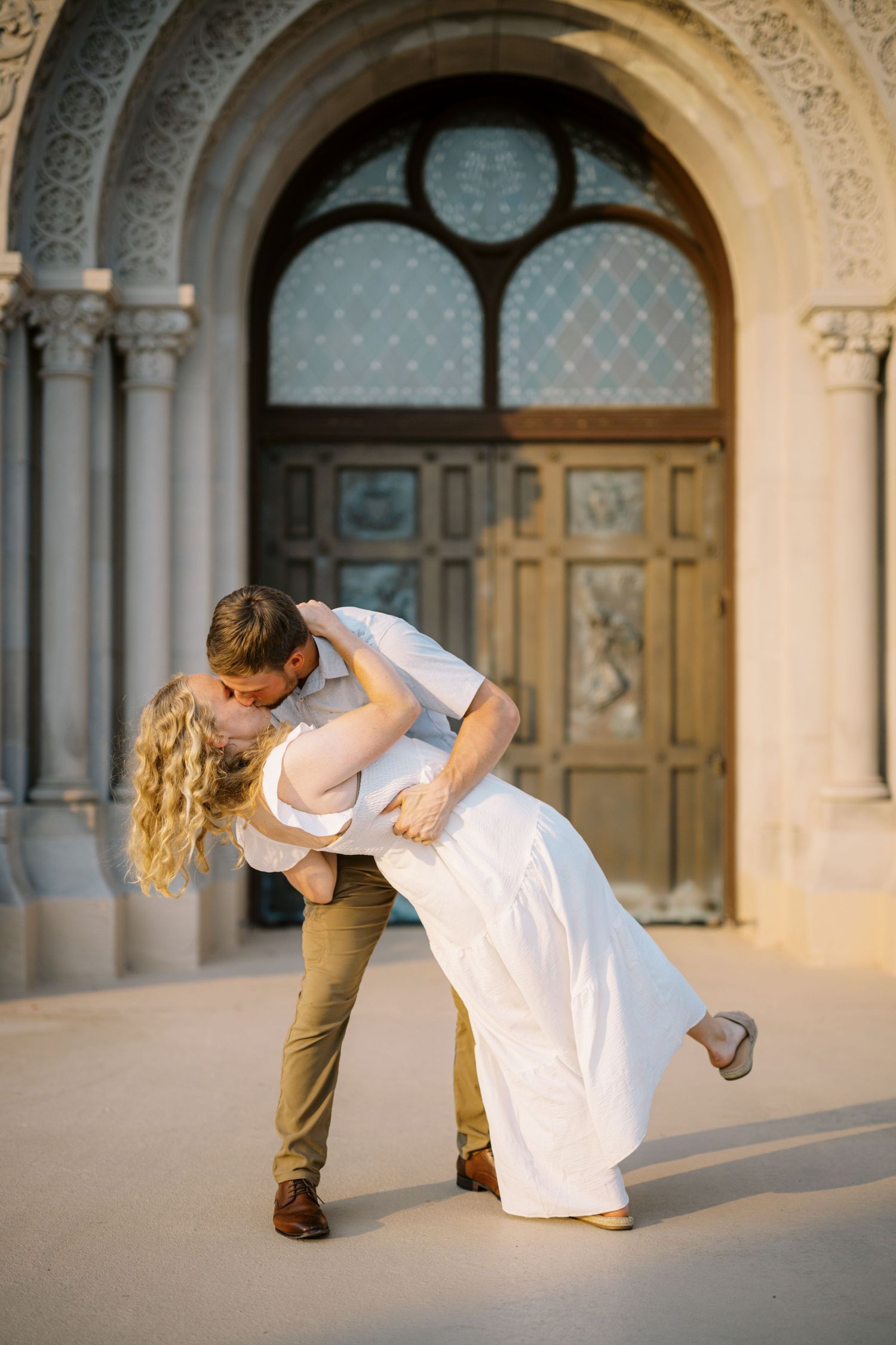 A romantic dip pose in front of an ornate arched doorway with a couple in wedding attire.