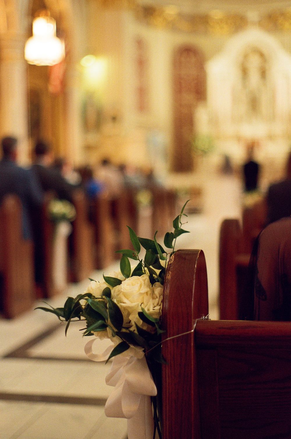 White roses bouquet decorating a church pew during a wedding ceremony with guests seated in the background.