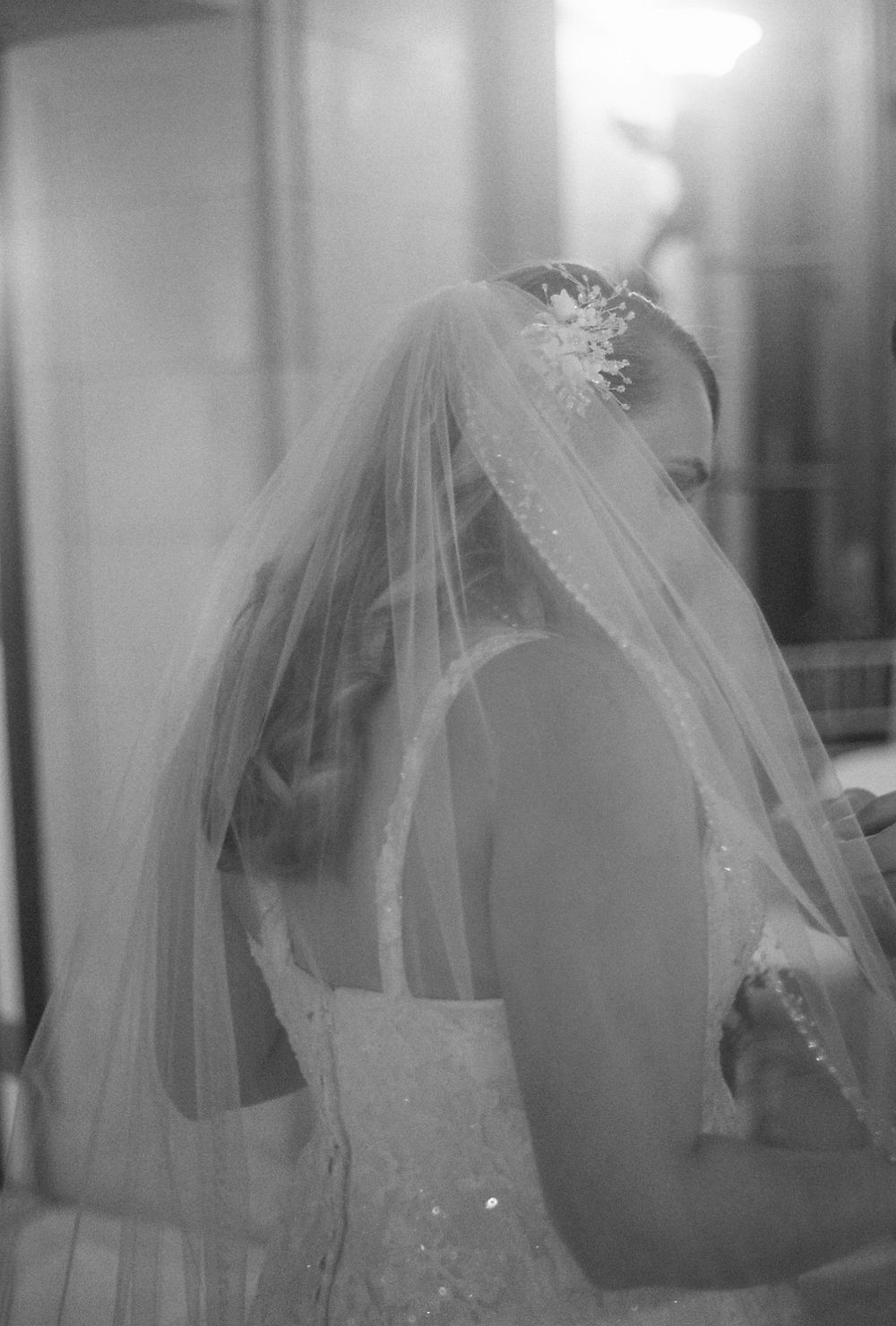 A bride's silhouette is captured in black and white through a delicate veil.