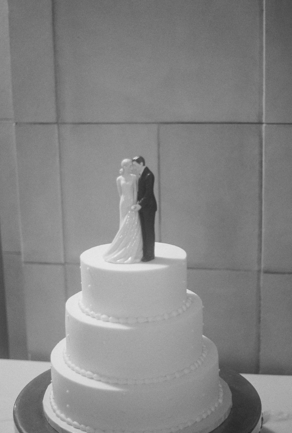 A classic white tiered wedding cake topped with a traditional bride and groom figurine topper in black and white at mansion in Rhode Island
