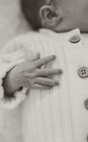 Close-up of tiny hand touching white knitted sweater with buttons.