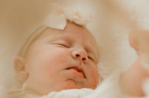 Peaceful sleeping newborn with soft bow headband in dreamy lighting.