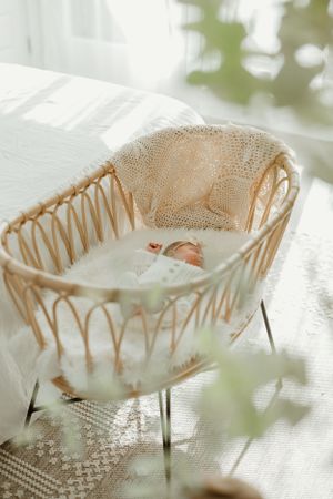 Newborn sleeping peacefully in vintage-style woven bassinet with soft natural lighting.