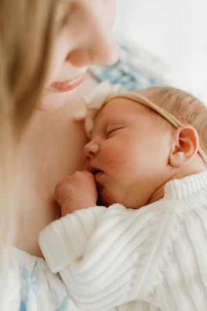 Tender moment with sleeping newborn wearing white onesie and delicate headband.
