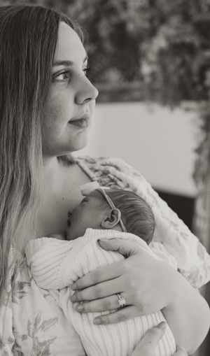 A tender black and white portrait of a parent gazing sideways while holding a sleeping infant.