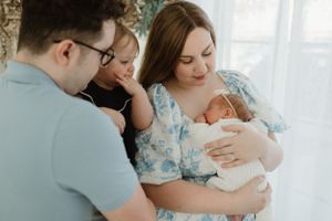 An intimate family moment as parents gather around their newborn baby in a bright room.