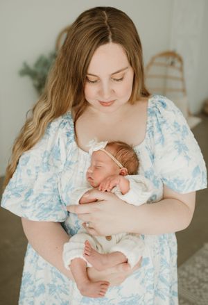 Parent in a blue floral dress lovingly cradling a sleeping newborn against their chest.