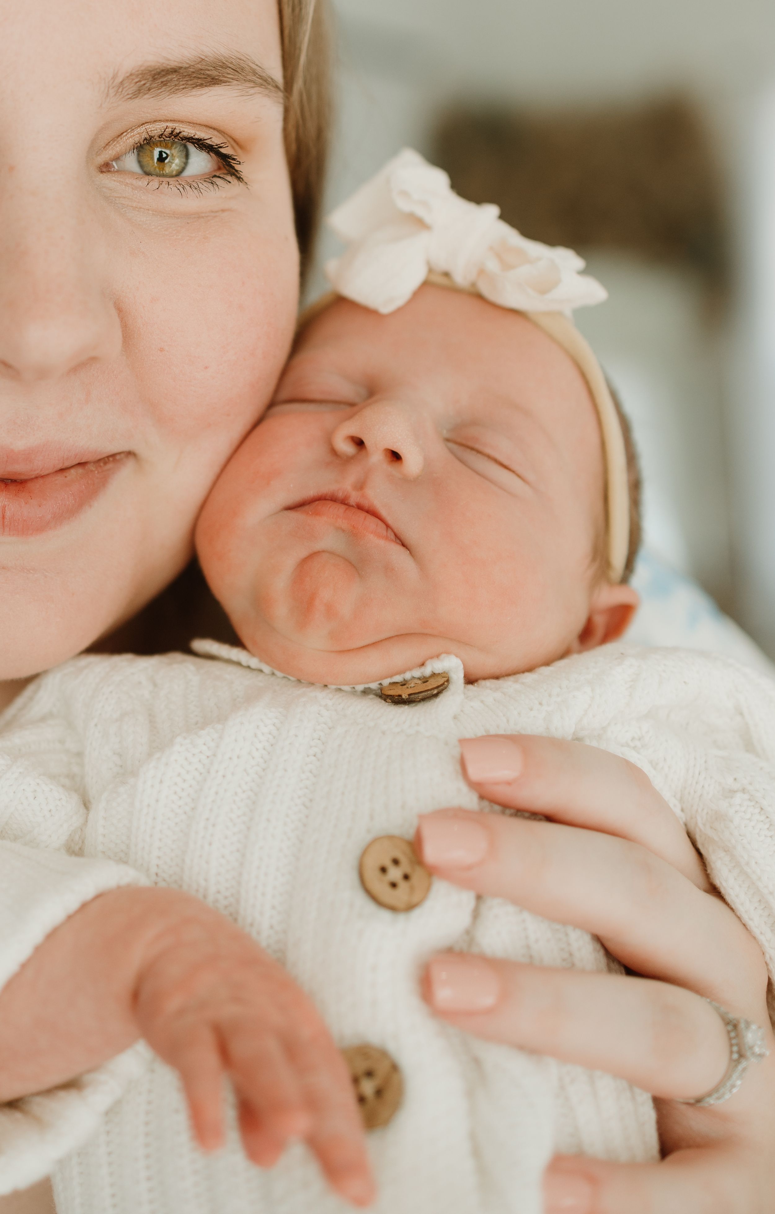 Close-up portrait of a sleeping baby in white clothing with a decorative bow headband.