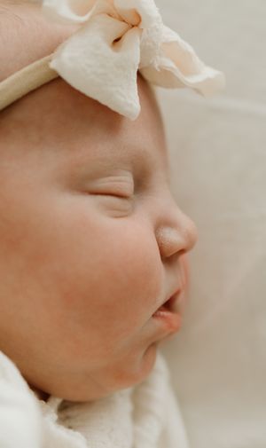 Peaceful close-up profile of a sleeping infant wearing a white bow.