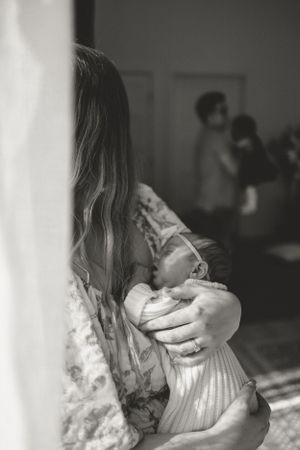 Black and white image of parent holding infant in striped clothing near a window.
