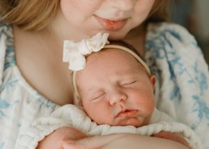 Sleeping newborn with white bow headband resting peacefully against floral dress.