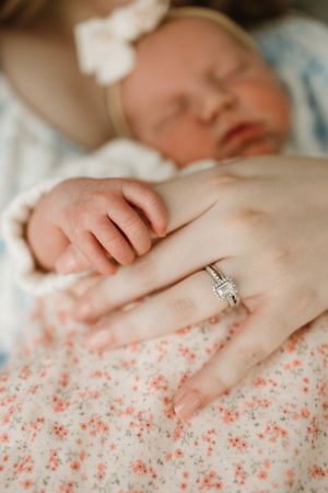Close-up of sleeping baby's hand near engagement ring on floral fabric.