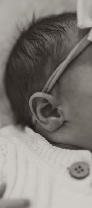 Close up black and white detail of a baby's ear and dark wispy hair.