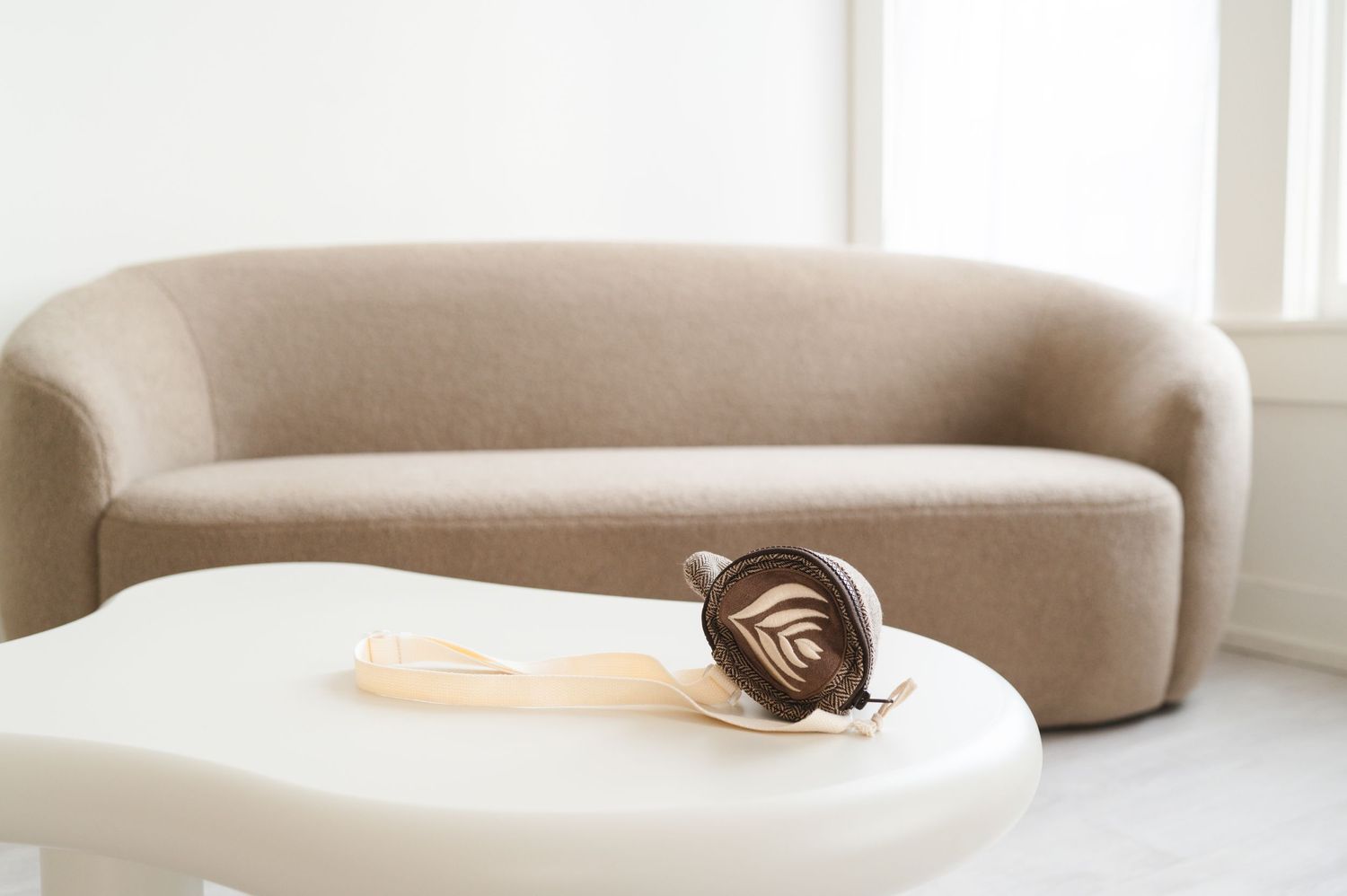 An elegant brown rose lies on a white modern coffee table with a curved beige sofa in the background.