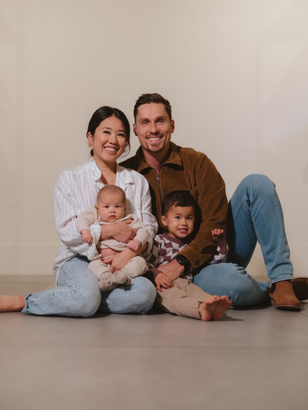 A casual family portrait with everyone sitting on the floor in coordinated casual outfits.