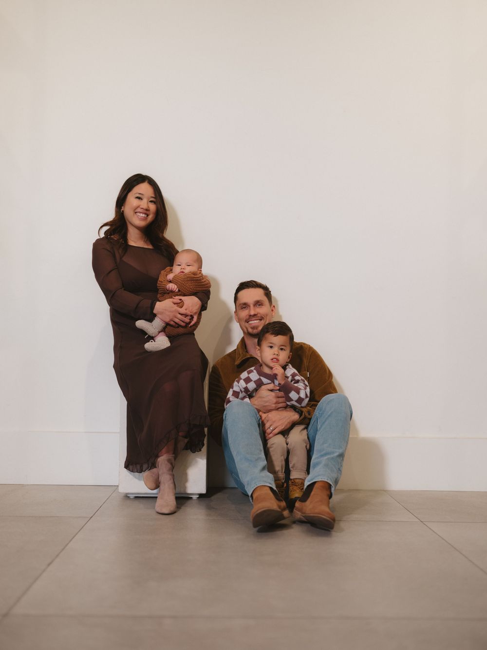 A relaxed family portrait with parents and children sitting on a light colored floor.