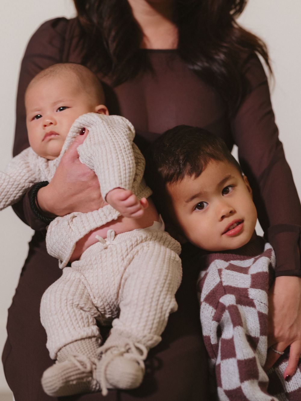 A family portrait showing a baby in white and a toddler in checkered attire with their caregiver.