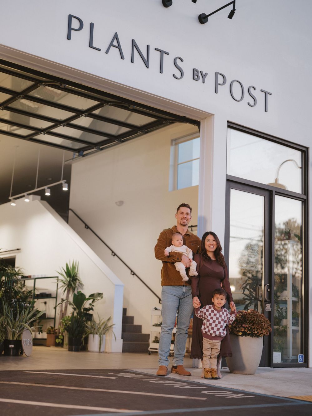 A family stands together outside a modern plant shop with large glass windows and indoor greenery.