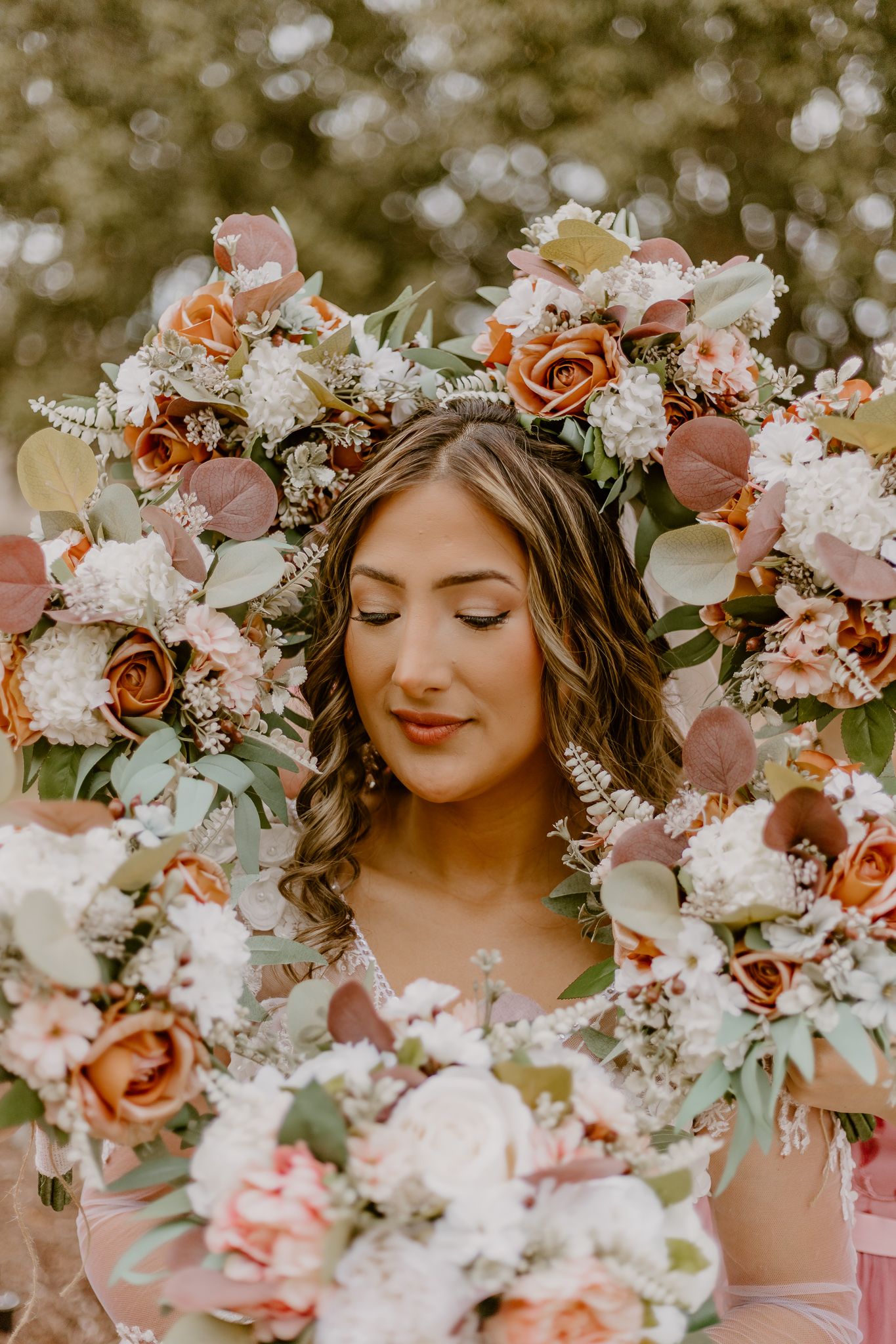 Close-up portrait surrounded by lush peach and pink floral arrangements in romantic outdoor setting.