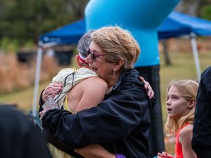 Emotional embrace between participants at an outdoor event under a blue tent.