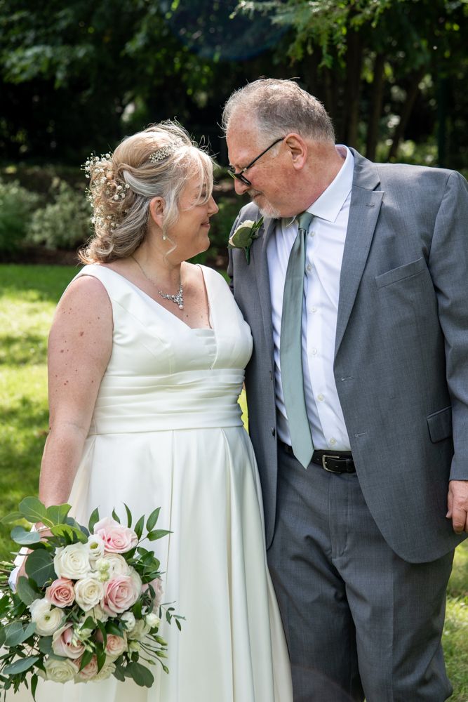 Couple sharing intimate moment outdoors with pink and white bouquet at garden wedding.