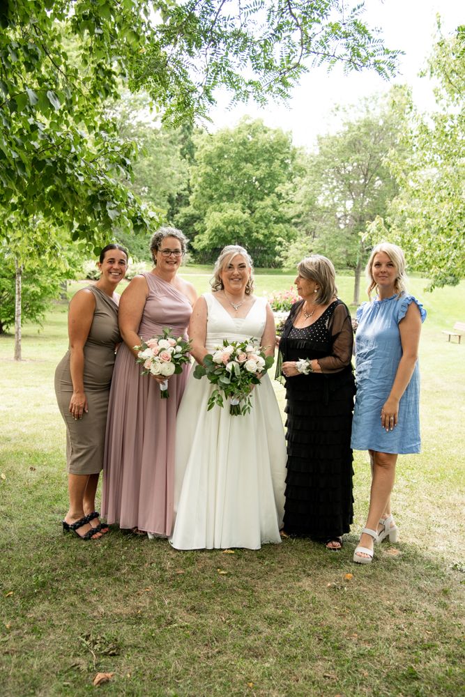 A bride in white surrounded by family in mauve and formal attire poses in a garden.