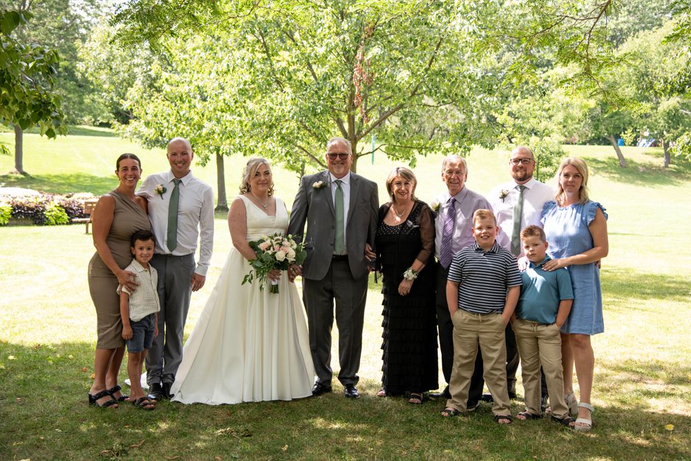 Wedding family poses together under shady trees in a summer garden setting.