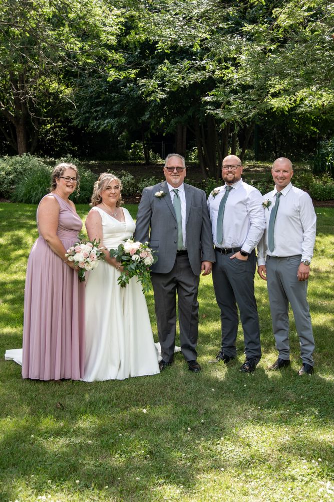 A bridal party poses for formal photos in a lush garden setting.