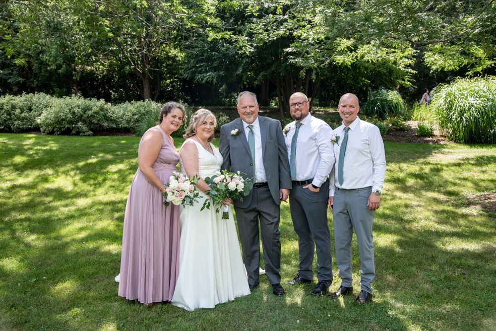A small wedding party poses together on a sunny lawn with trees in the background.