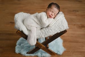 Sleeping newborn wrapped in white knit blanket on wooden bench with blue accent.