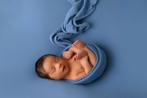 Peaceful newborn draped in flowing blue fabric during artistic portrait session.