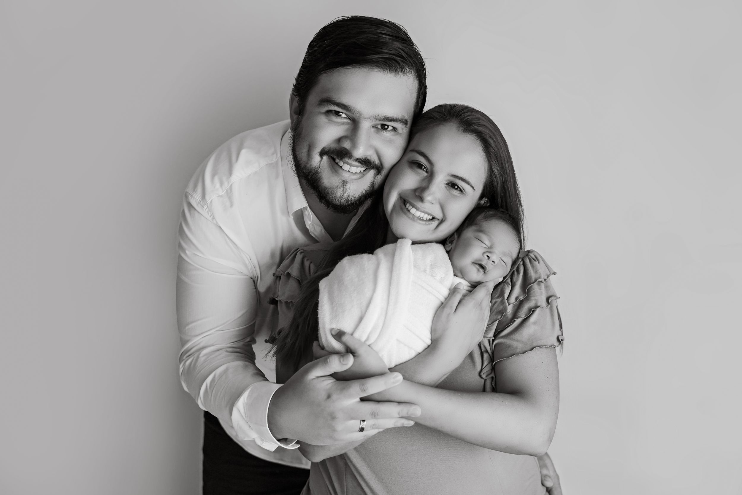 Black and white portrait of loving family embracing against neutral background.