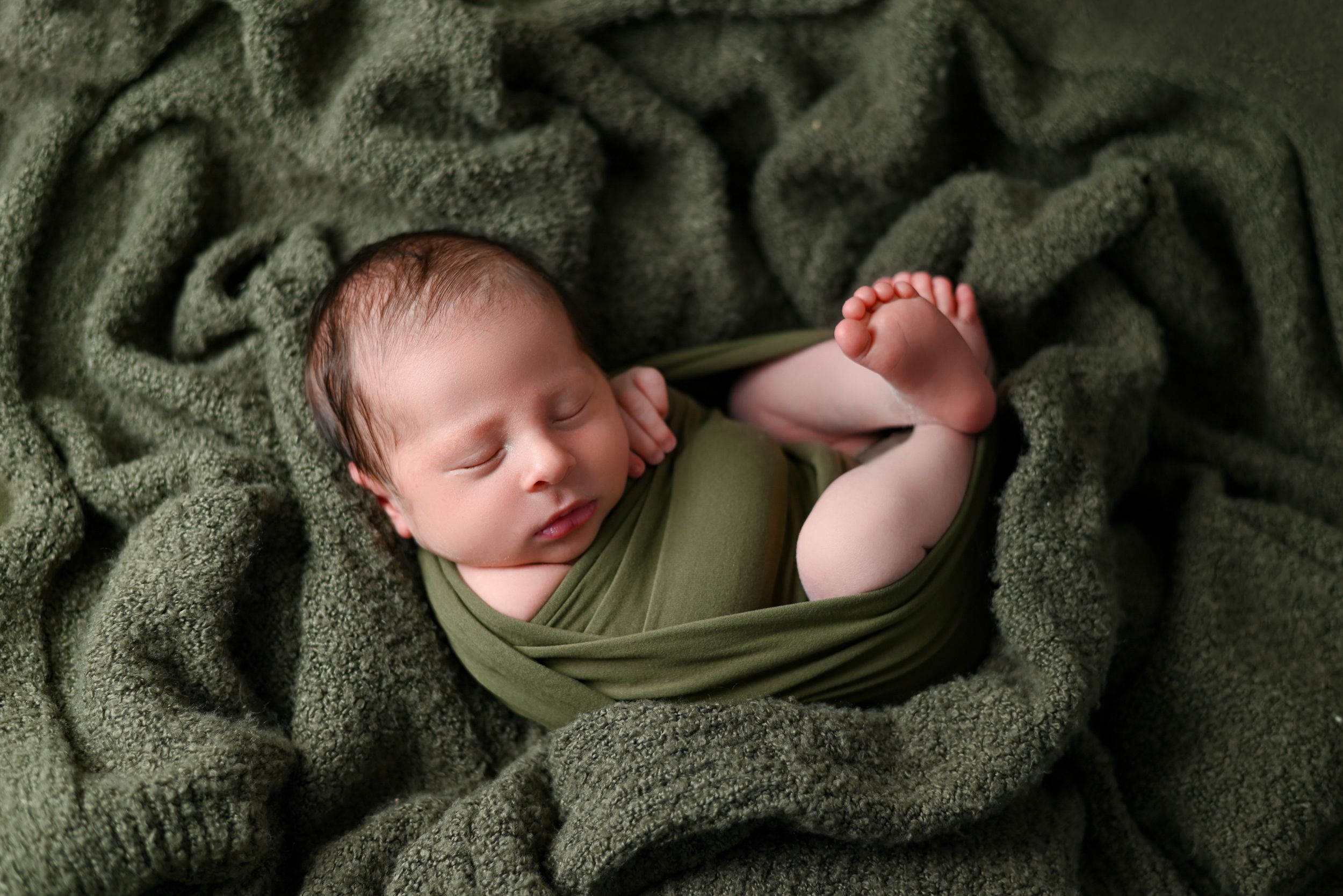 Sleeping newborn wrapped in olive green blanket during cozy portrait session.