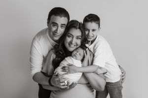 Family of four embracing in black and white studio portrait.