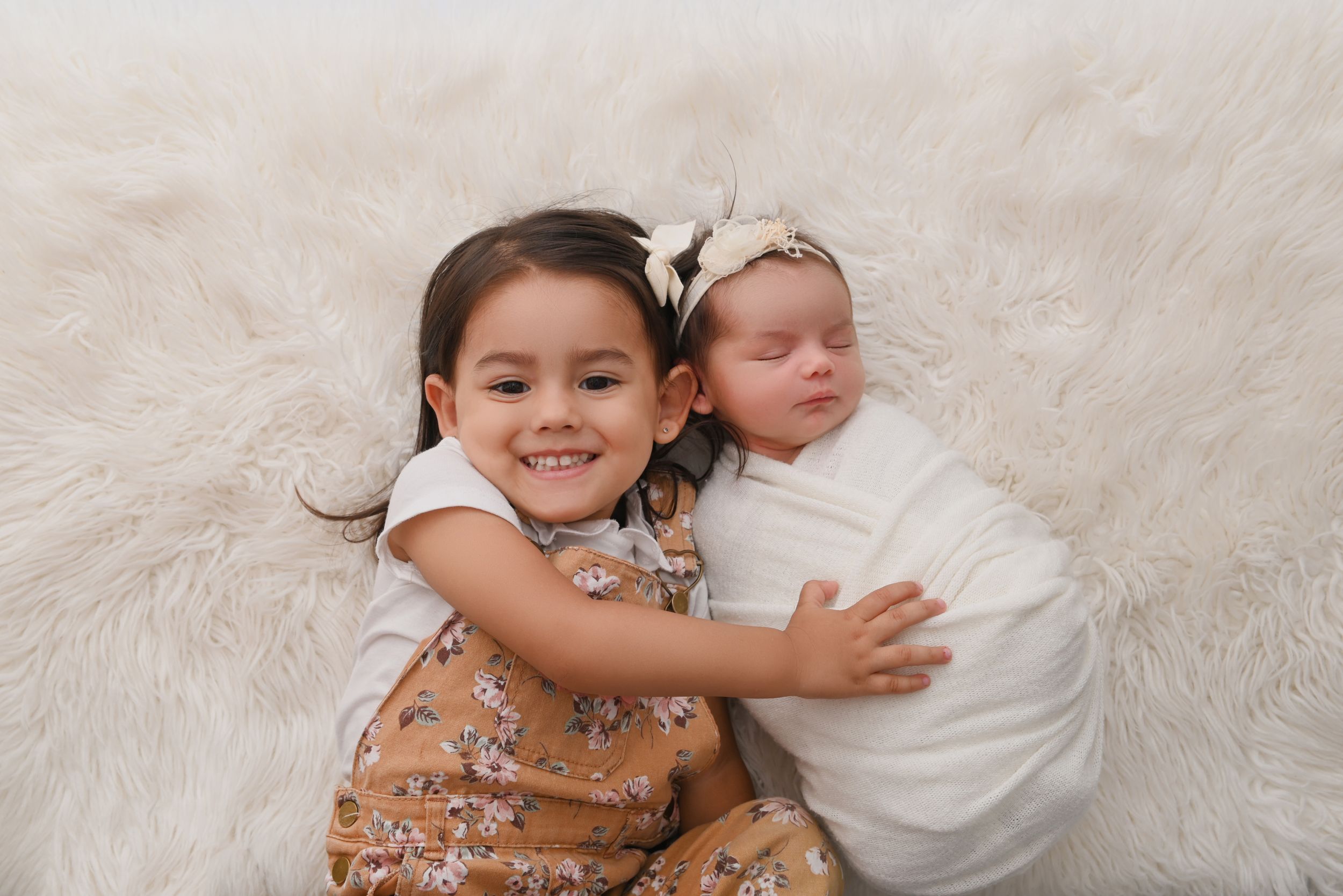 Two children lying on white fur rug during studio portrait session.
