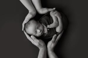 Black and white photograph showing tiny newborn cradled in gentle hands against dark background.
