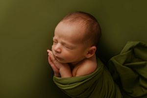 Sleeping newborn wrapped in olive green fabric during professional photo session.
