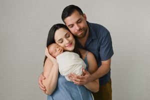 Couple embracing while wearing casual clothing against neutral gray backdrop.