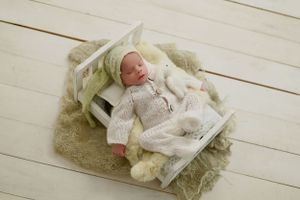 Newborn wearing white outfit lying in vintage wooden crate with textured fabric.